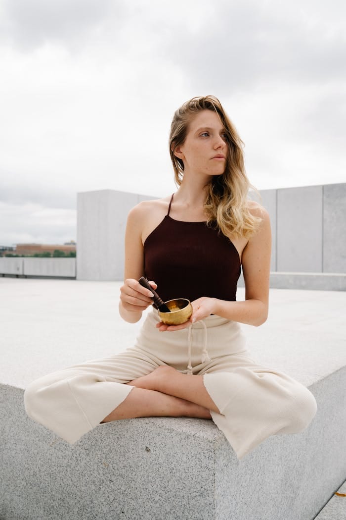 A woman meditates outdoors, holding a Tibetan singing bowl, promoting wellness and mindfulness.