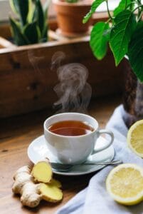 Escena de autocuidado en casa: taza de té digestivo de hierbas, rodajas de jengibre y limón sobre mesa de madera, plantas verdes, luz cálida natural, ambiente relajante y acogedor, estilo editorial wellness, alta calidad, sin texto.